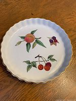 Top-down view of the white ceramic pan showing the colorful fruit design of peach, cherries, and berries.
