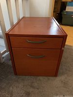 Front view of wood filing cabinet showing two drawers with metal handles and lock on the side.