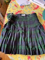 Front view of the pleated Black Watch tartan kilt showing two silver-tone buckles and straps for fastening.