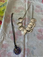 Both necklaces laid flat, showing the silver hammered necklace and the black leather rope with glass pendant.