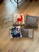 Five decorative pillows arranged on floor showing various designs and colors.