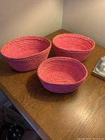 All three pink wicker baskets arranged on a wooden surface displaying size differences