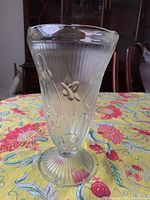 Pressed glass vase showing vertical ribbed texture and raised iris floral design on clear glass.