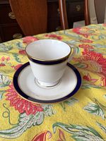 Close-up image of one tea cup placed on the matching saucer showing the cobalt blue band rim with gold accents and the white porcelain interior and body.