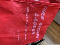 Close-up of red carrying bag with white text 'Fire Escape Ladder' and manufacturer information.