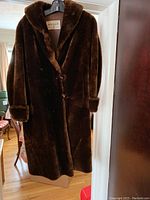 Full view of vintage brown sheared beaver fur coat hanging, showing mid-length design with lapels and buttons.