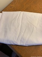 Folded white textured round tablecloth on wooden surface