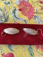 Pair of elongated marquise-shaped sterling silver West Coast Aboriginal art earrings on red velvet background.