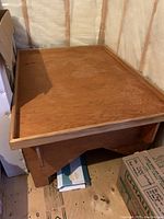 Wooden train table in a storage or unfinished room area; showing top surface and raised edges from an angle.