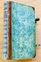 Front board showing green marbled paper cover, brown leather spine and corner caps, metal clasps