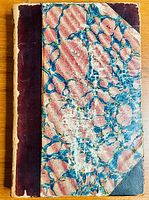 Full view of the book front cover showing marbled pink and blue design with dark brown leather spine and corners.