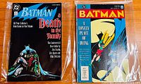 Two Batman graphic novel trade paperbacks in sealed plastic bags on wooden surface, front covers visible: Batman Death in the Family and Batman A Lonely Place of Dying.