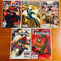 Five Nightwing comic books displayed fan-like on a wooden surface showing front covers highlighting characters and circus themes