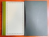 Front cover of the book with green spine and decorative border on cream cover, alongside a black slipcase.