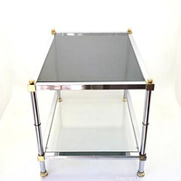 Front angle view showing smoked glass top, clear glass bottom shelf, chrome tubular frame with brass corner caps and ball finials.