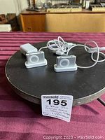 Two Apple iPod Shuffles on their charging stations with cables visible on black circular surface with auction lot tag.