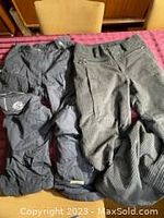 Two pairs of snowboard pants lying on a table, one black and one charcoal colored corduroy.