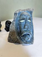 Front view of the large stone figural carving showing carved face with white inlaid eyes and detailed facial features