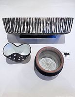 Large rectangular ceramic flower pot with textured black and white striped exterior, greenish interior, next to two smaller vessels on a white surface.