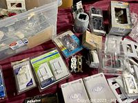 Bin with assorted light switches, dimmer switches, outlet receptacles, conduit boxes, wall plates, locks, handles, and curtain rod brackets seen packed loosely with new and used items.