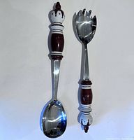 Set of two salad servers with brown and white ceramic handles and stainless steel functional parts, laid flat on white background.