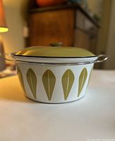 Side view of pot with lid showing green Lotus pattern on white enamel.