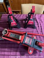 Photo of the red Motomaster 2.25 ton hydraulic car jack with long handle, placed with two black Motomaster 3 ton car stands showing the entire lot.