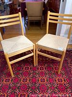 Pair of oak wood mid-century modern chairs photographed sitting on a red patterned rug with rope woven seats and ladder backs.