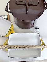 Top-down view of three pieces together: brown stock pot, yellow casserole, and loaf pan, with measuring ruler to indicate size