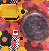 Three items on patterned fabric background: teak platter with intricate dark wood layers, yellow & black Terraillon scale with rectangular pan, and colorful fabric runner