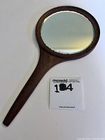 Top view of mid-century teak hand mirror showing oval mirror glass and long wooden handle.