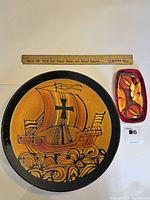 Large round plate with Viking ship design and black border with wooden ruler above showing size.