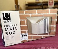 Box showing the Umbra Postino Mailbox branding with product image and brushed stainless steel finish.