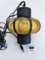 Close-up of amber bubble glass shade with black metal frame, electrical cord and plug visible.