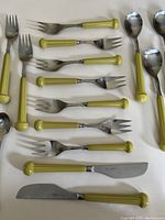 Close-up of knives and forks with yellow-green ceramic handles, stainless steel blades and tines, arranged on a white background.