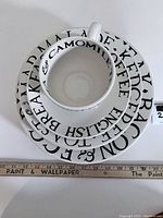 Top view of stacked cup, saucer, and dinner plate showing typographic black text on white ceramic.