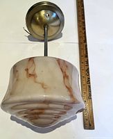 Front view of the vintage glass globe pendant light with ruler for size reference showing the pinkish, marbled swirl pattern on the glass globe and metal mounting base.