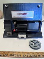 Front open view of the Kalart EV-8 Mark II Editor Viewer with film reel in foreground and demonstrating the viewer's film editing mechanism and viewer screen.