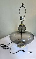 Full view of the large vintage smoke glass and brass table lamp showing the glass body and brass base with harp and finial.