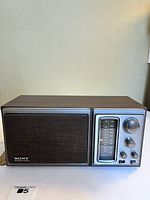 Front view of the vintage Sony radio showing wood grain finish, speaker cover, tuning dial, and knobs.