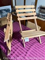 Two wooden pop-up chairs shown upright on a table with a purple cloth, highlighting the slatted seat and backrest design.