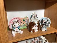 Six ceramic animal figurines arranged on a shelf including cat, dog, birds, and duck shapes.