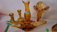 All five amber colored art glass pieces displayed together including two vases, two candlestick holders, and a centerpiece bowl.