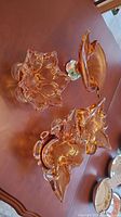 Four amber art glass pieces displayed on table showing varied shapes and sizes, with clear glass accents and ruffled edges.