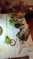 Five green art glass pieces arranged on a white tablecloth including a lidded compote, ruffled dishes, bud vase, and long dish.