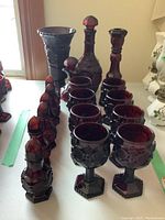 View of entire set showing eight glasses, three sets of salt and pepper shakers, two cruets, and one vase in ruby glass with textured design.