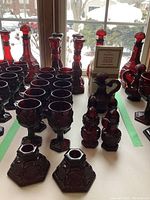 Full view of over 20 pieces of ruby red glassware, including decanters, goblets, salt and pepper shakers, flower vases, and candle holders.