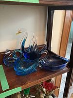 Four blue glass bird figurines displayed on a wooden shelf showing different angles and group arrangement.