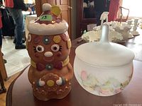 Photo showing gingerbread lady cookie jar with colorful icing details and floral glass bowl with frosted surface and painted flowers.