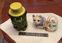 Green puppy cookie jar with yellow hat and bow tie, white cat cookie jar with brown stripes and blue bow tie, side view with measurement scale.
